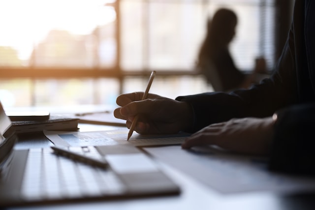 close up view of businessman hand holding pen writing on paperwork at his office desk