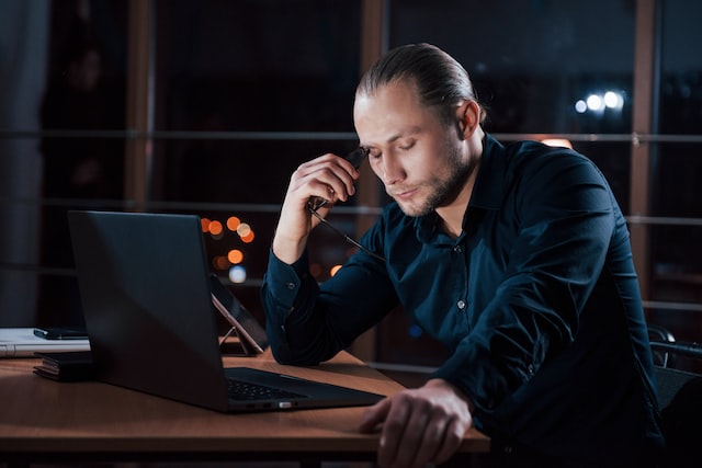 stylish businessman in eyewear sits alone in the office at nightime