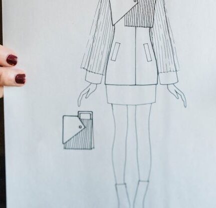 Lifestyle Trends - Crop unrecognizable female fashion designer wearing casual clothes demonstrating paper with drawing of new creative model of jacket and purse