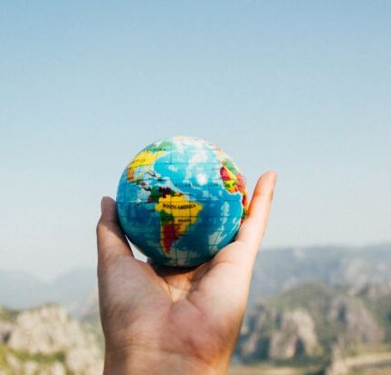 Traveling - Person Holding World Globe Facing Mountain