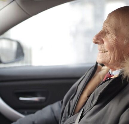 Travel Insurance - Side view of content elderly male in suit and outerwear sitting in front seat of contemporary automobile and looking away