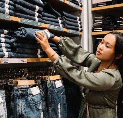 Ethical Clothing - Woman Looking at the Jeans on a Wooden Shelf