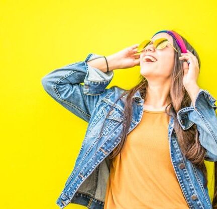 Fashion - Smiling Woman Looking Upright Standing Against Yellow Wall