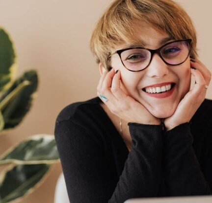 Corporate Responsibility - Cheerful woman smiling while sitting at table with laptop