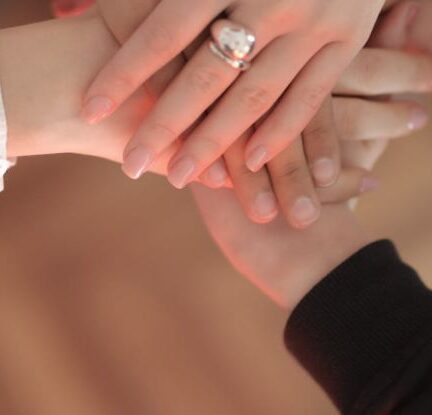 Community Engagement - Top view of faceless friends in different clothes stacking hands together while standing on wooden floor indoor on sunny day