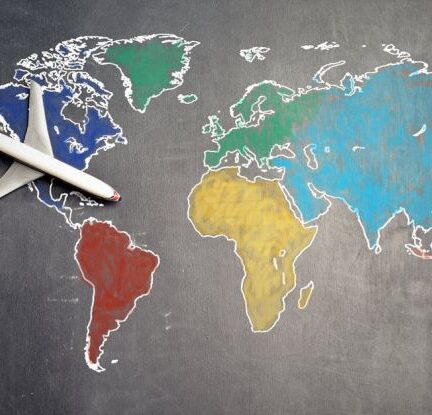 Globalization - Top view of crop anonymous person holding toy airplane on colorful world map drawn on chalkboard