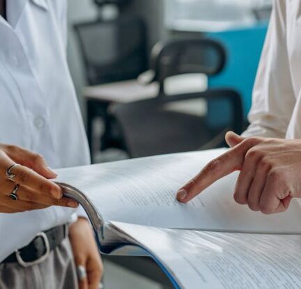 Finance Management - Colleagues Standing in White Long Sleeve Shirts Discussing and Reading a Financial Report