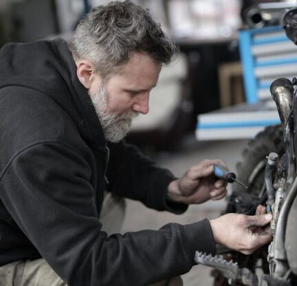 Vehicle Maintenance - Bearded man fixing motorcycle in workshop